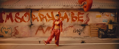 a man walking down a street in front of a graffiti covered wall