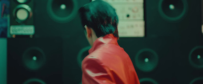 a man in a red jacket standing in front of a wall of speakers