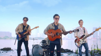 a group of young men playing guitars in front of a body of water