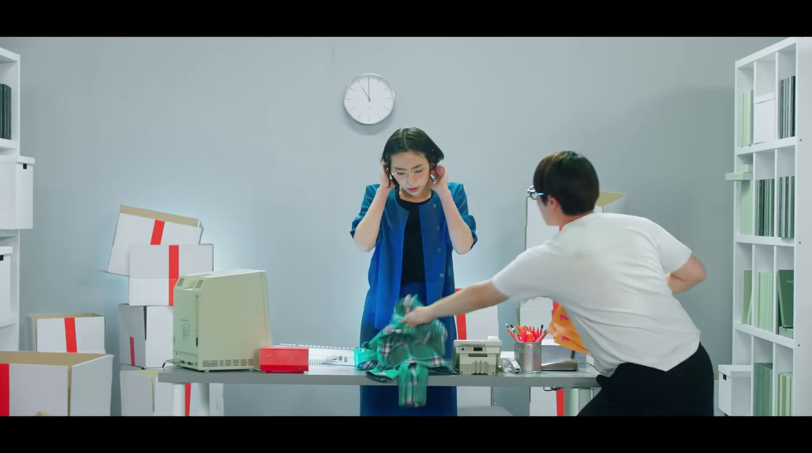 a man and woman in a room with boxes and a clock