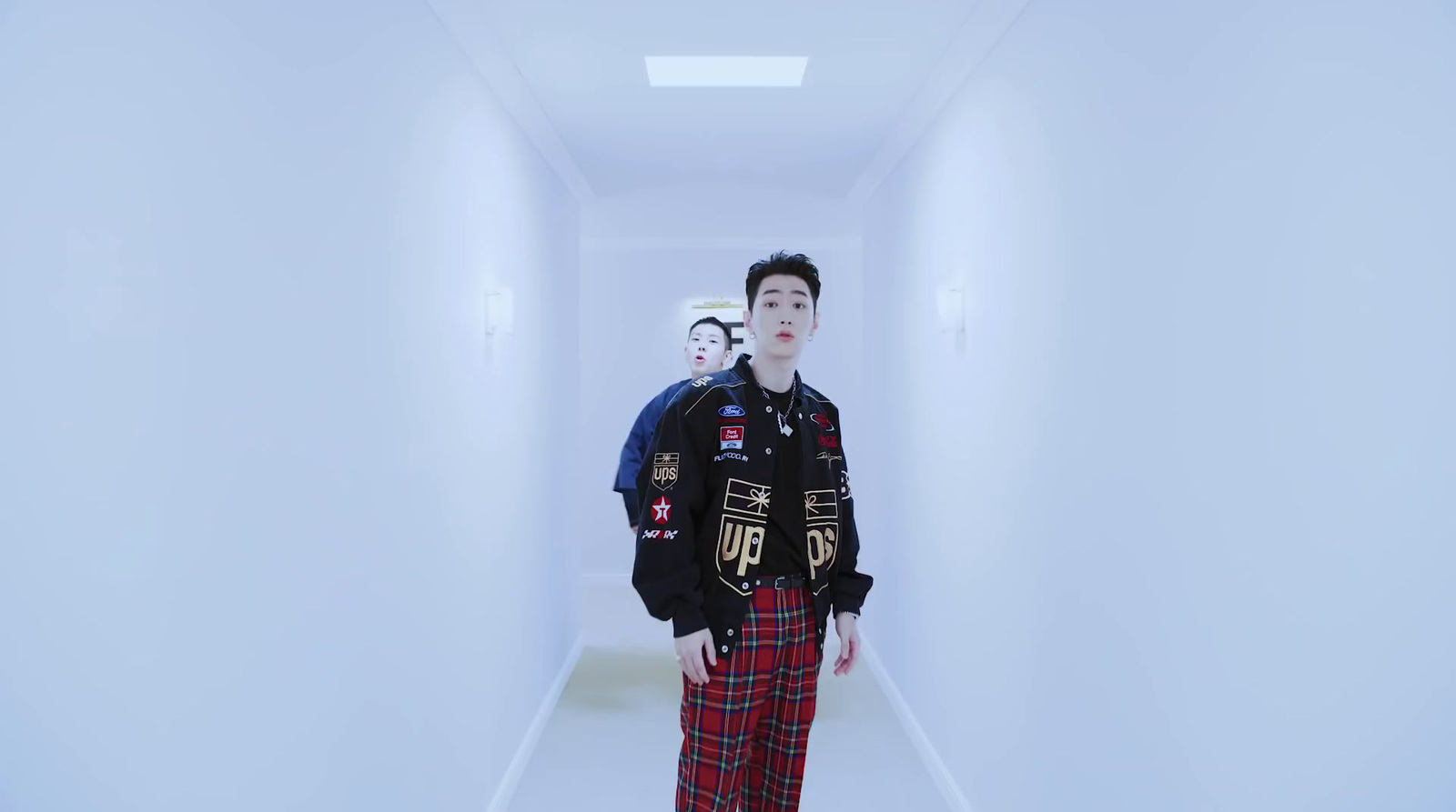 a man in a black jacket and plaid pants standing in a hallway