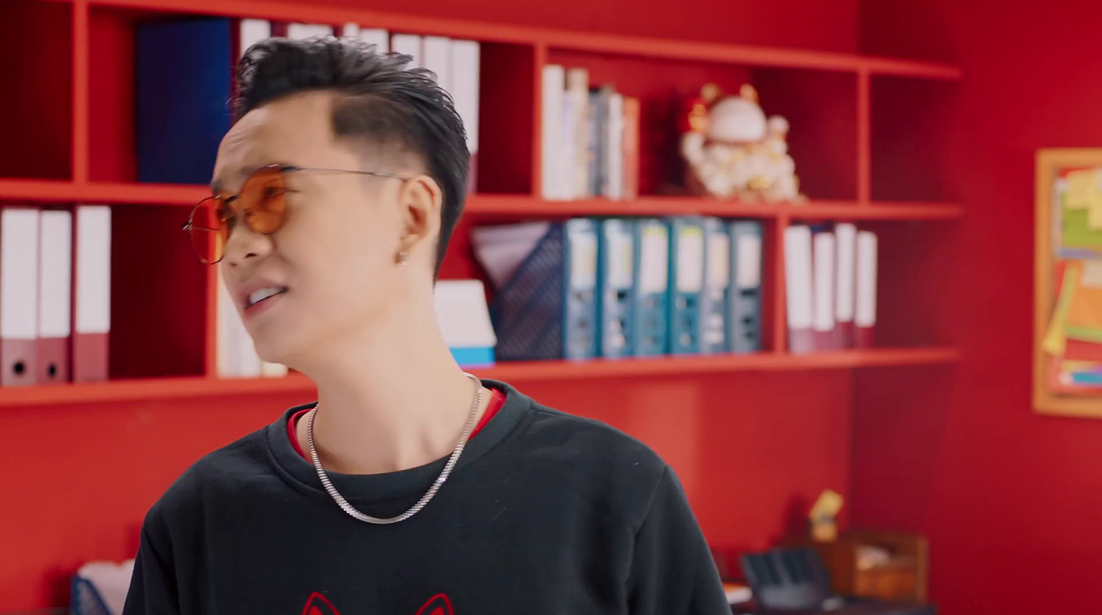 a young man wearing glasses standing in front of a bookshelf