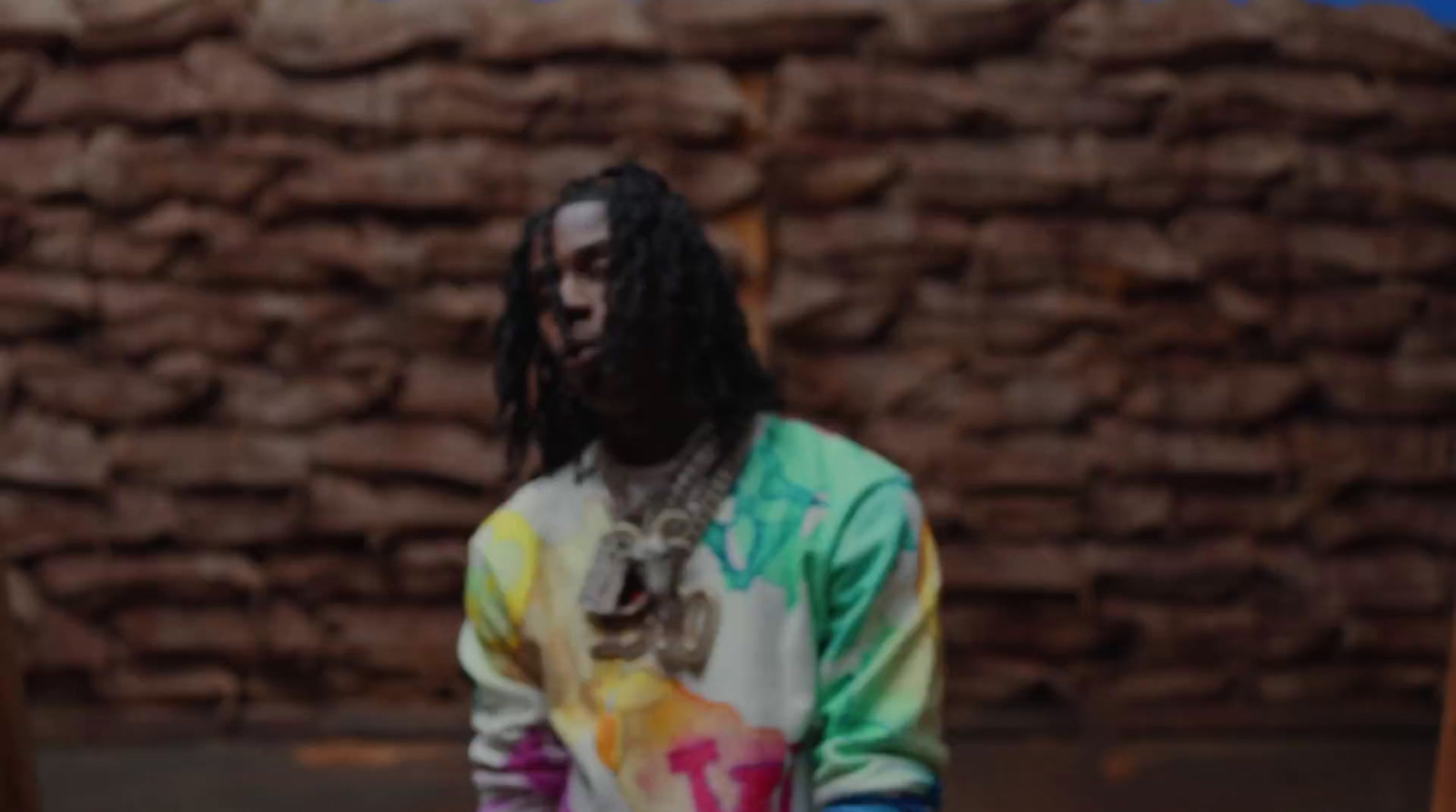 a man with dreadlocks standing in front of a brick wall