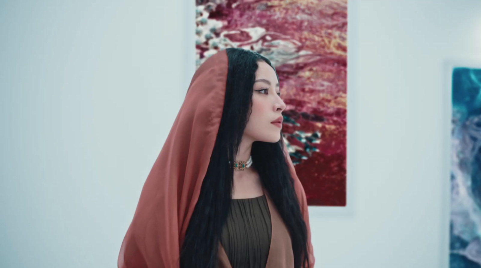 a woman with long black hair standing in front of a painting