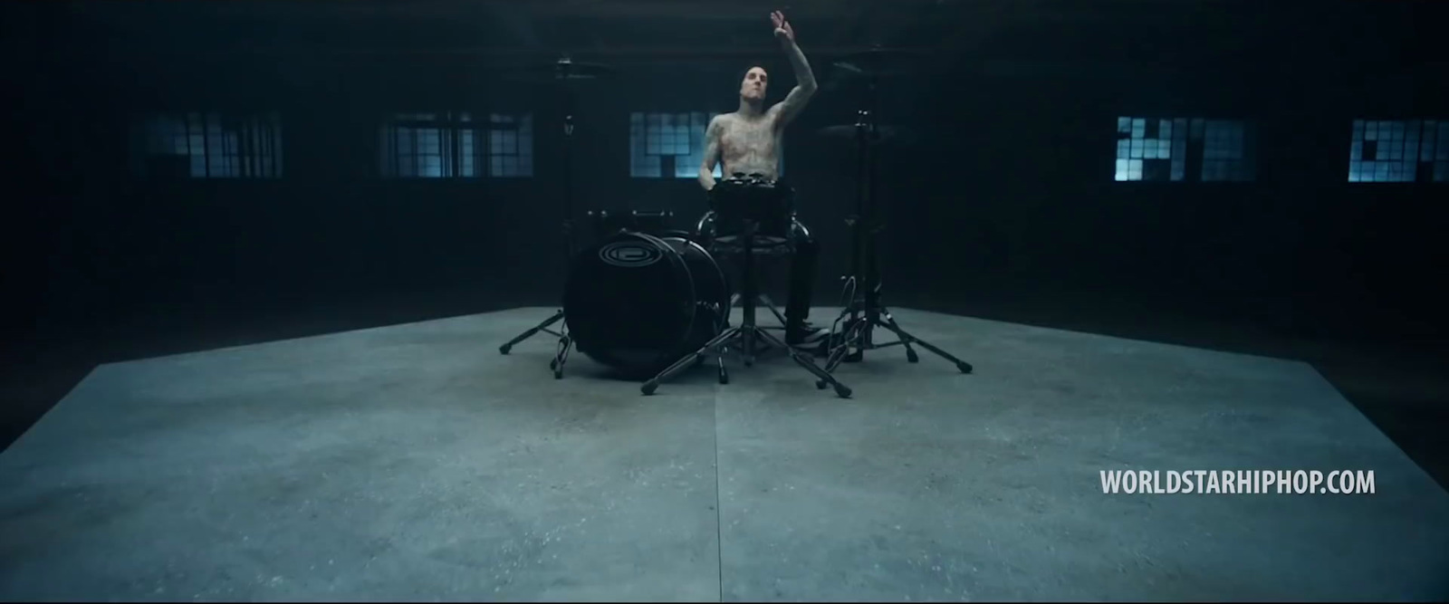 a shirtless man playing drums in a dark room