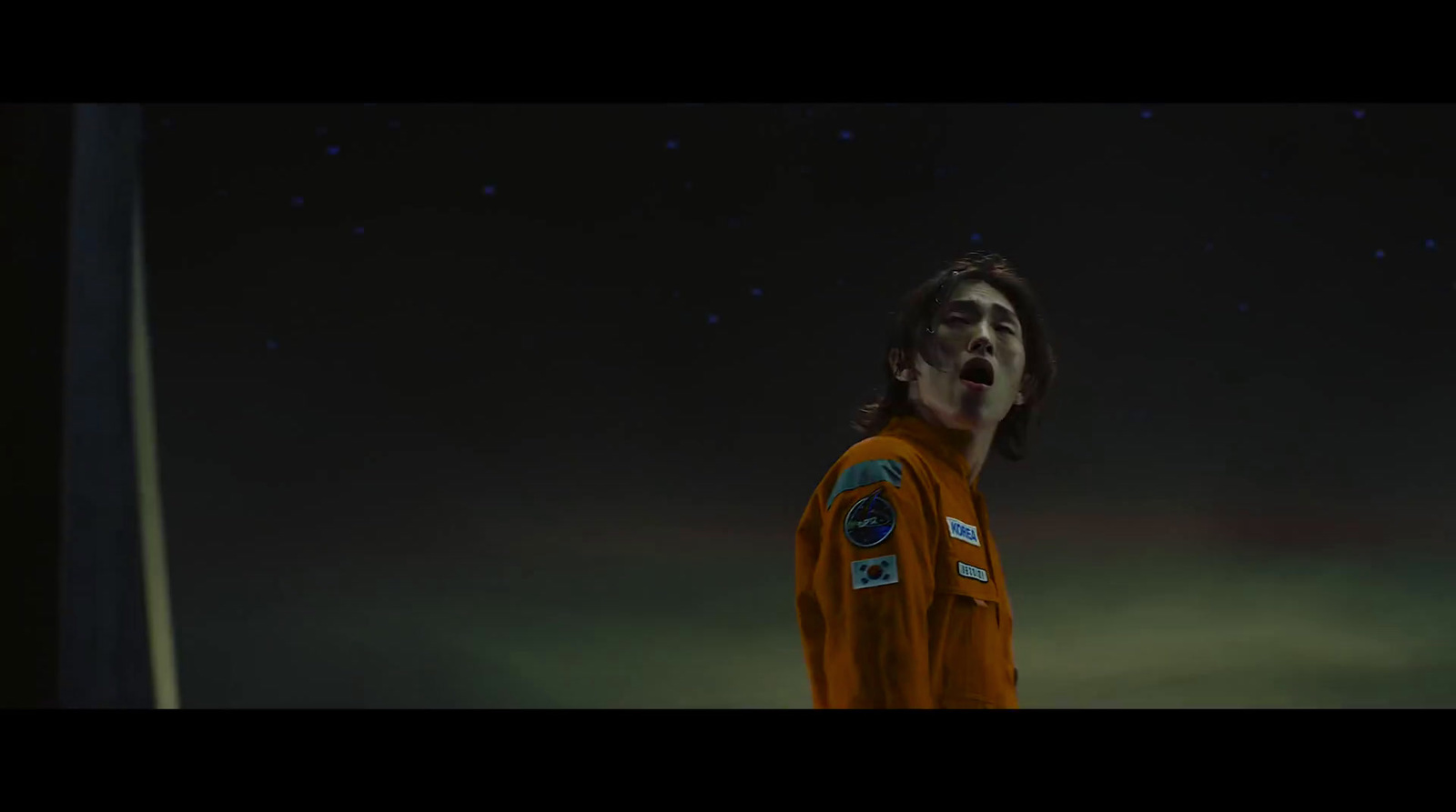 a man in an orange space suit standing in the dark