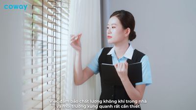 a woman standing next to a window with blinds