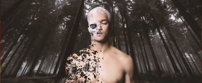 a shirtless man standing in a forest covered in black and white paint