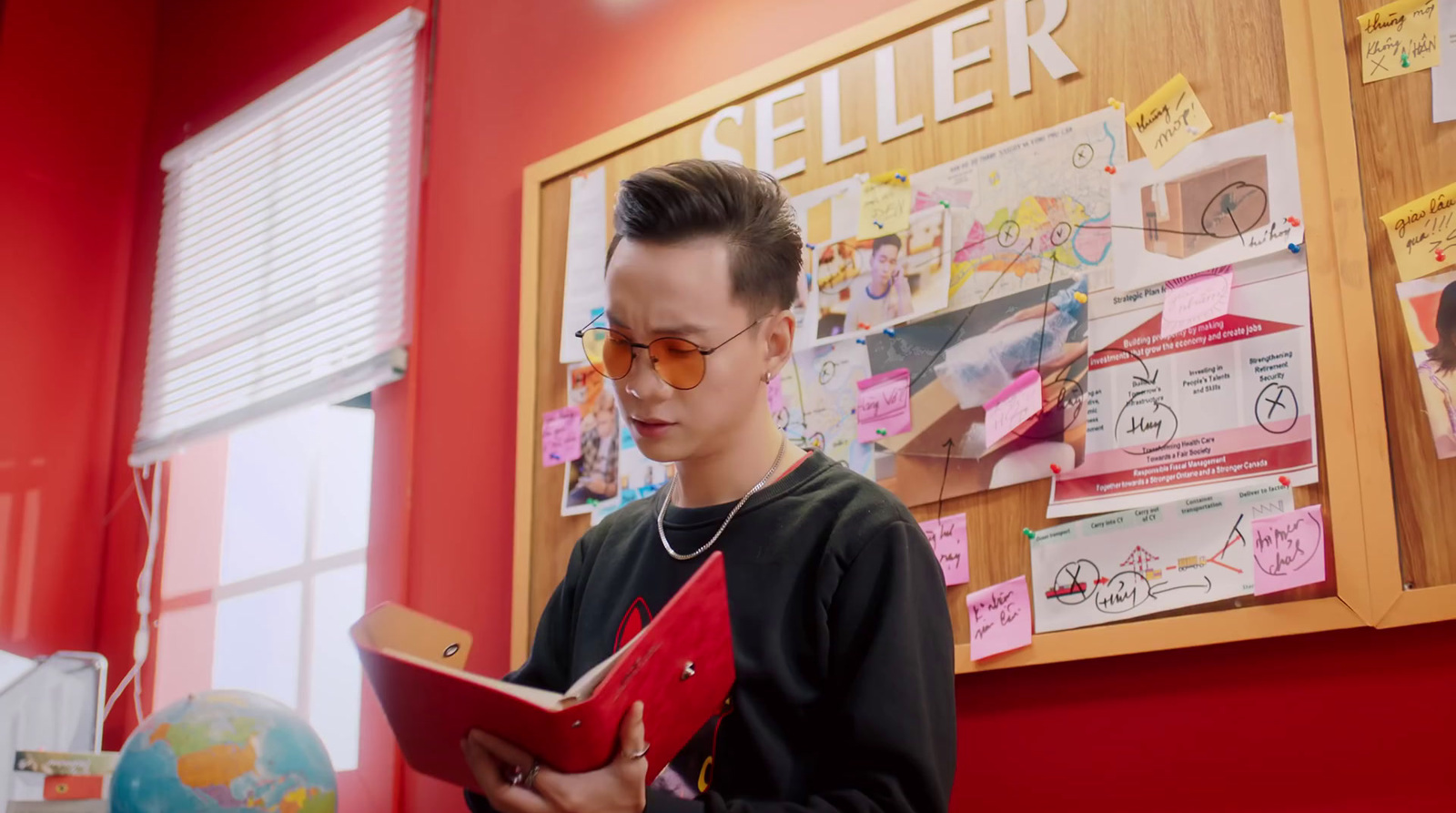 a young man is reading a book in front of a bulletin board