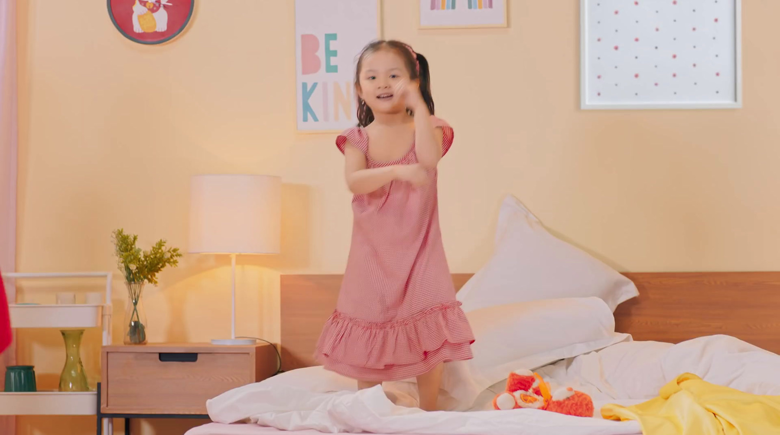 a little girl in a pink dress standing on a bed