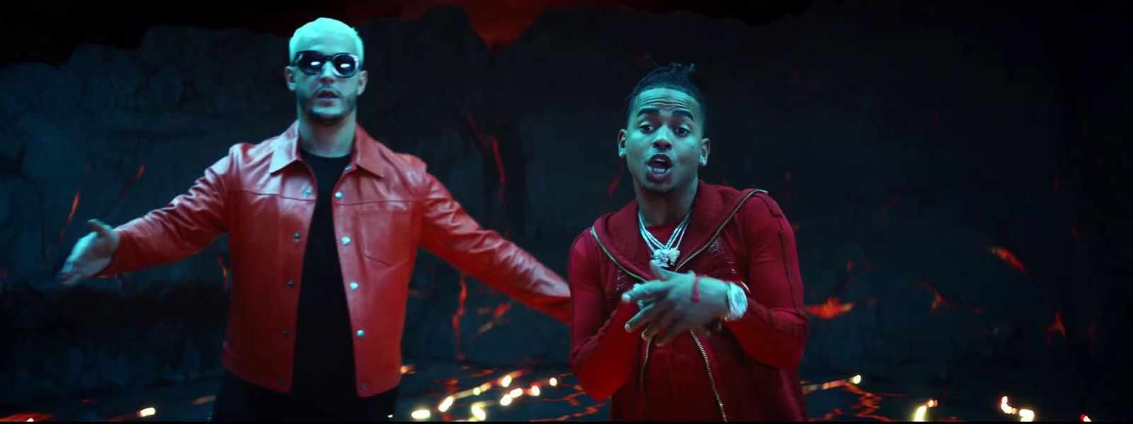 two men in red jackets are standing in front of a fire