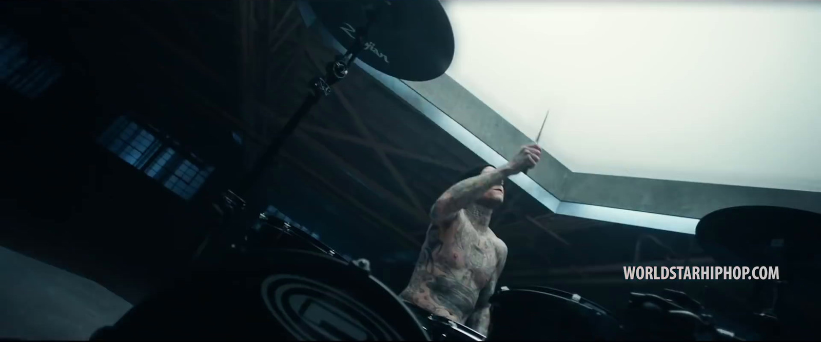 a shirtless man playing drums in a dark room