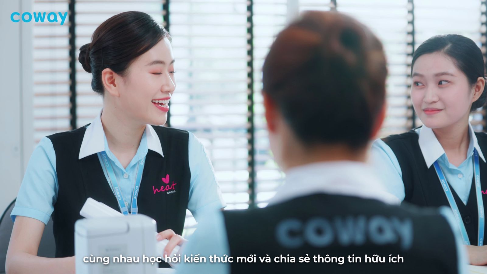 a woman sitting at a desk talking to another woman