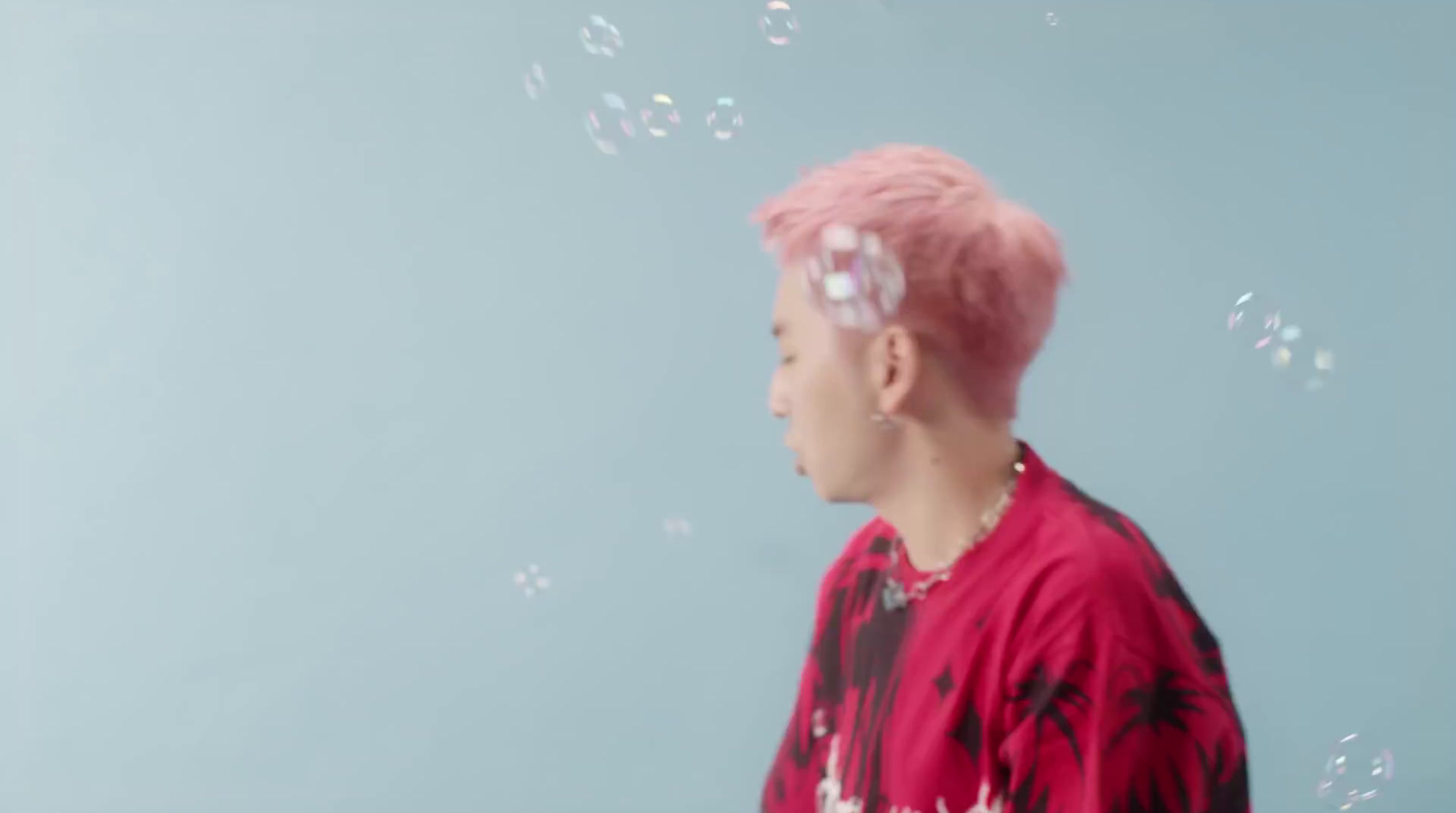 a man with pink hair blowing bubbles in the air