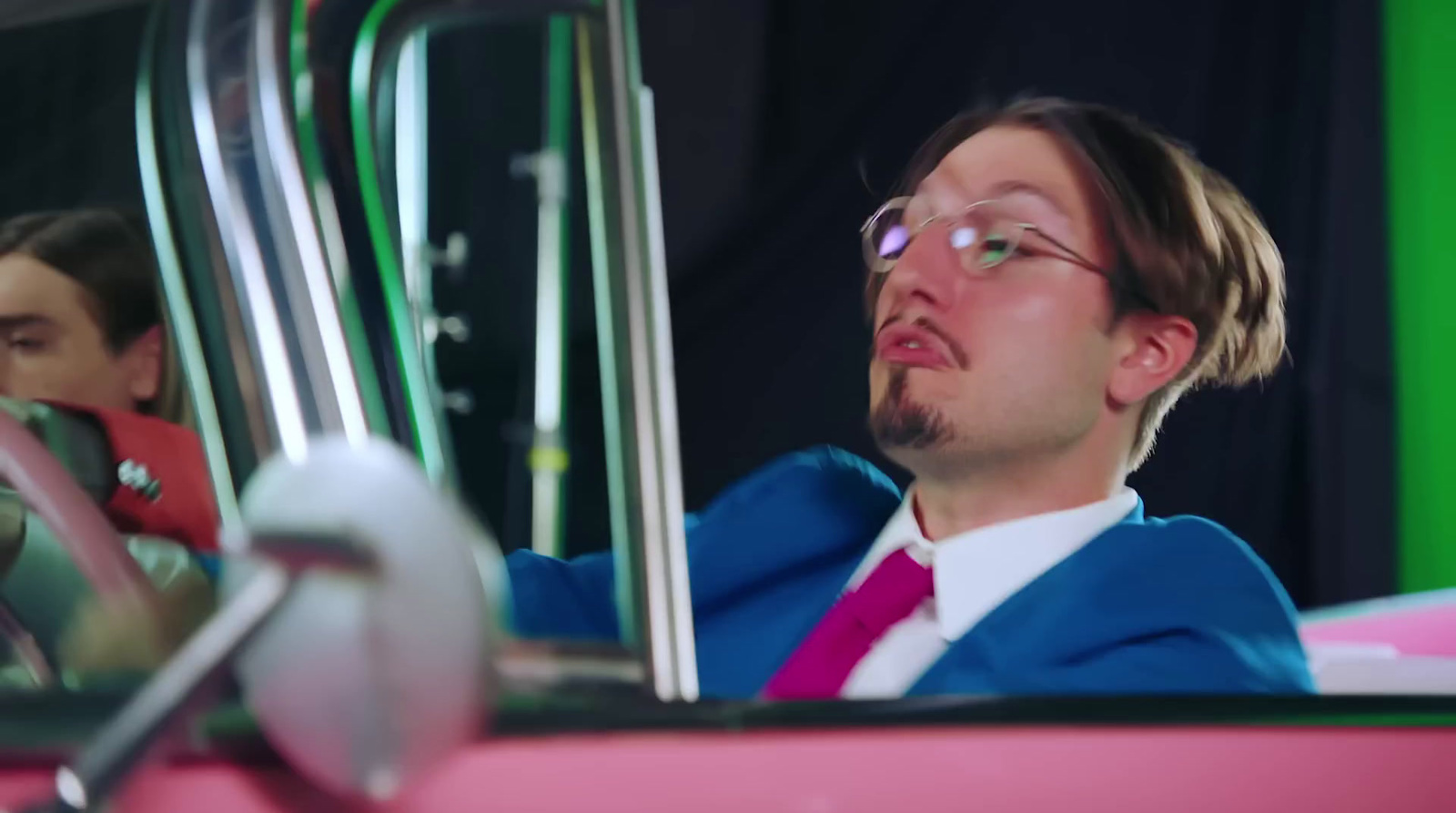 a man in a suit and tie sitting in a pink car