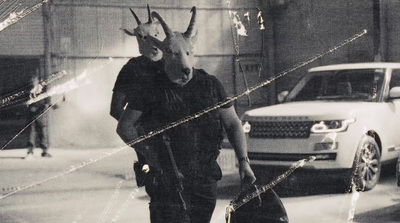 a man walking down a street with a goat mask on