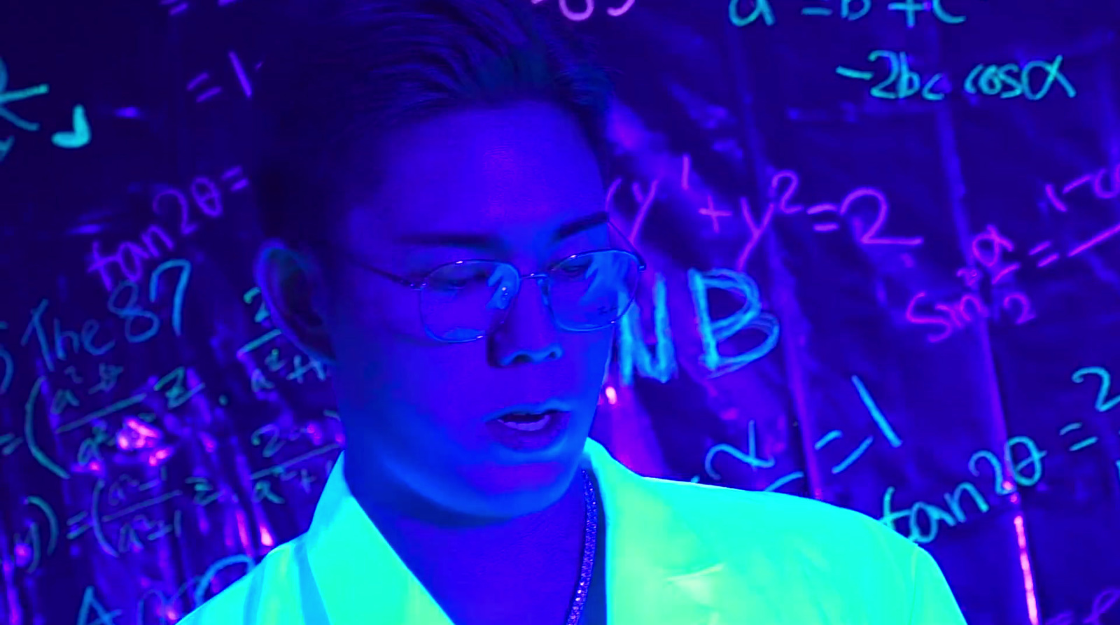 a man wearing glasses standing in front of a wall with writing on it