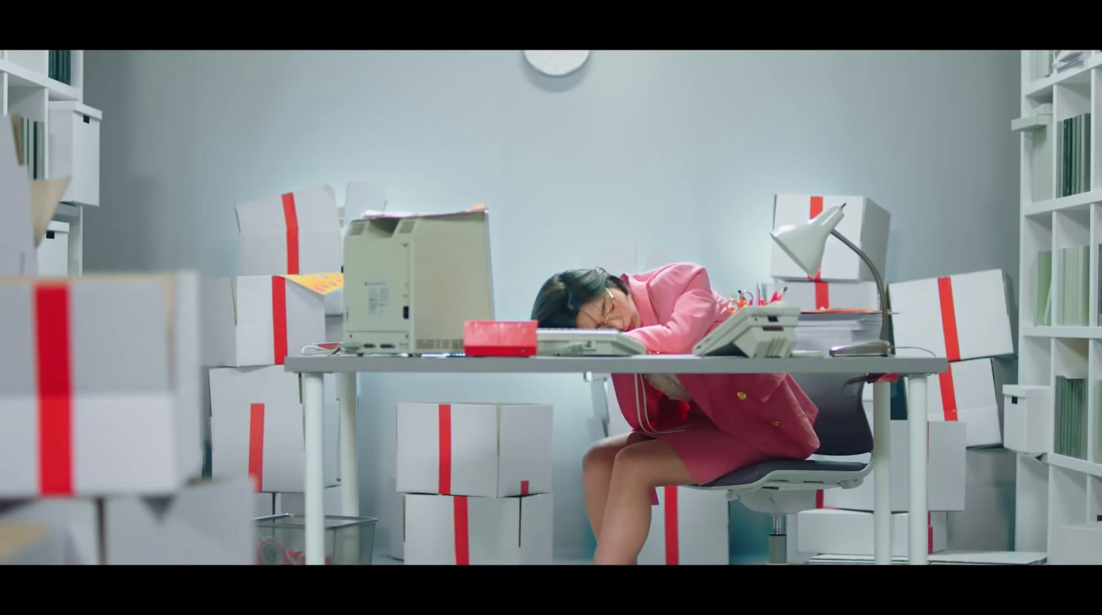 a woman sitting at a desk in a room filled with boxes