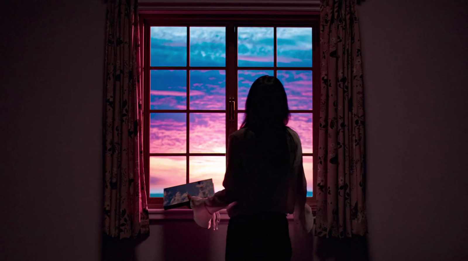 a woman standing in front of a window looking out at the sunset