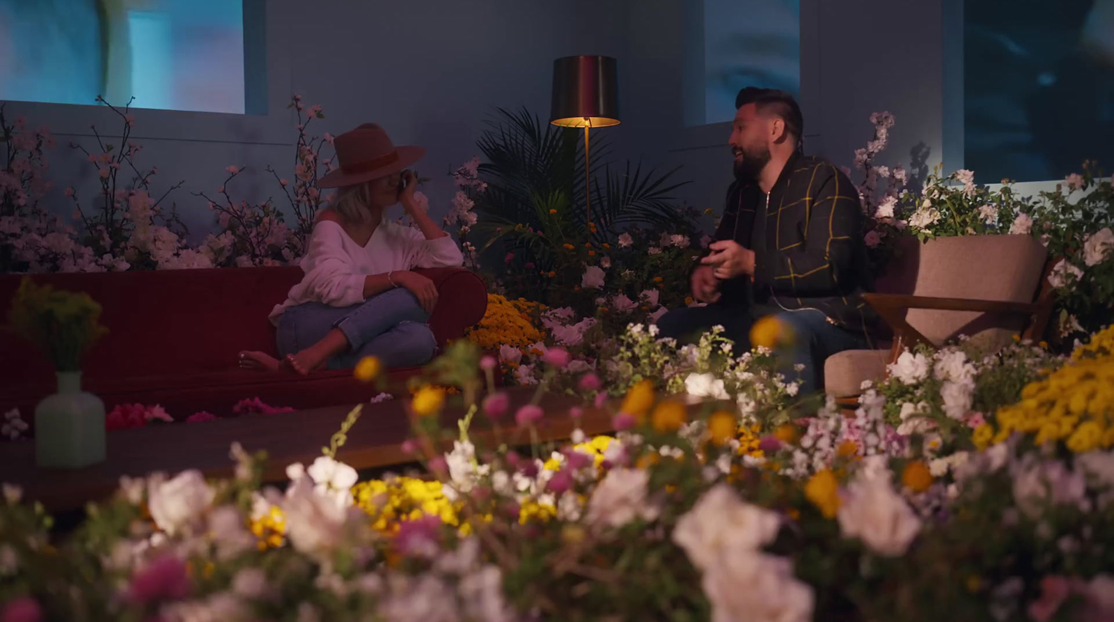 a man and a woman sitting on a couch in a room full of flowers