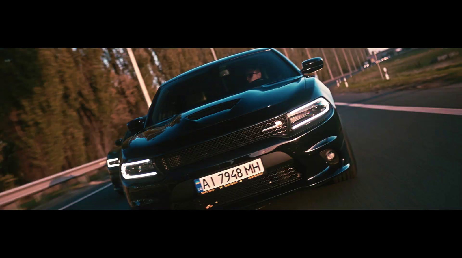 a black car driving down a road next to a forest