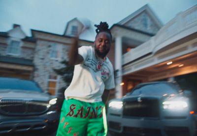 a man in a white shirt and green shorts standing in front of a car