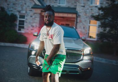 a man in a white shirt and green shorts standing in front of a car