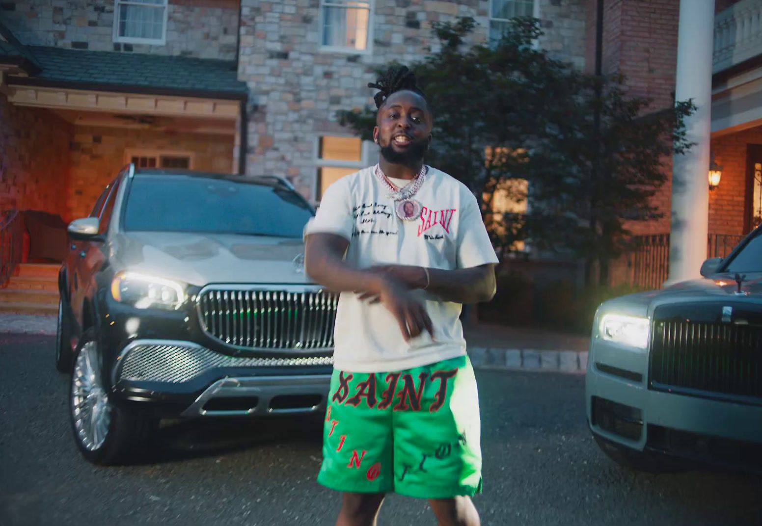 a man in a white shirt and green shorts standing in front of a car