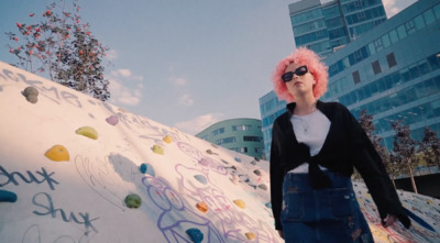 a woman with pink hair standing next to a rock wall