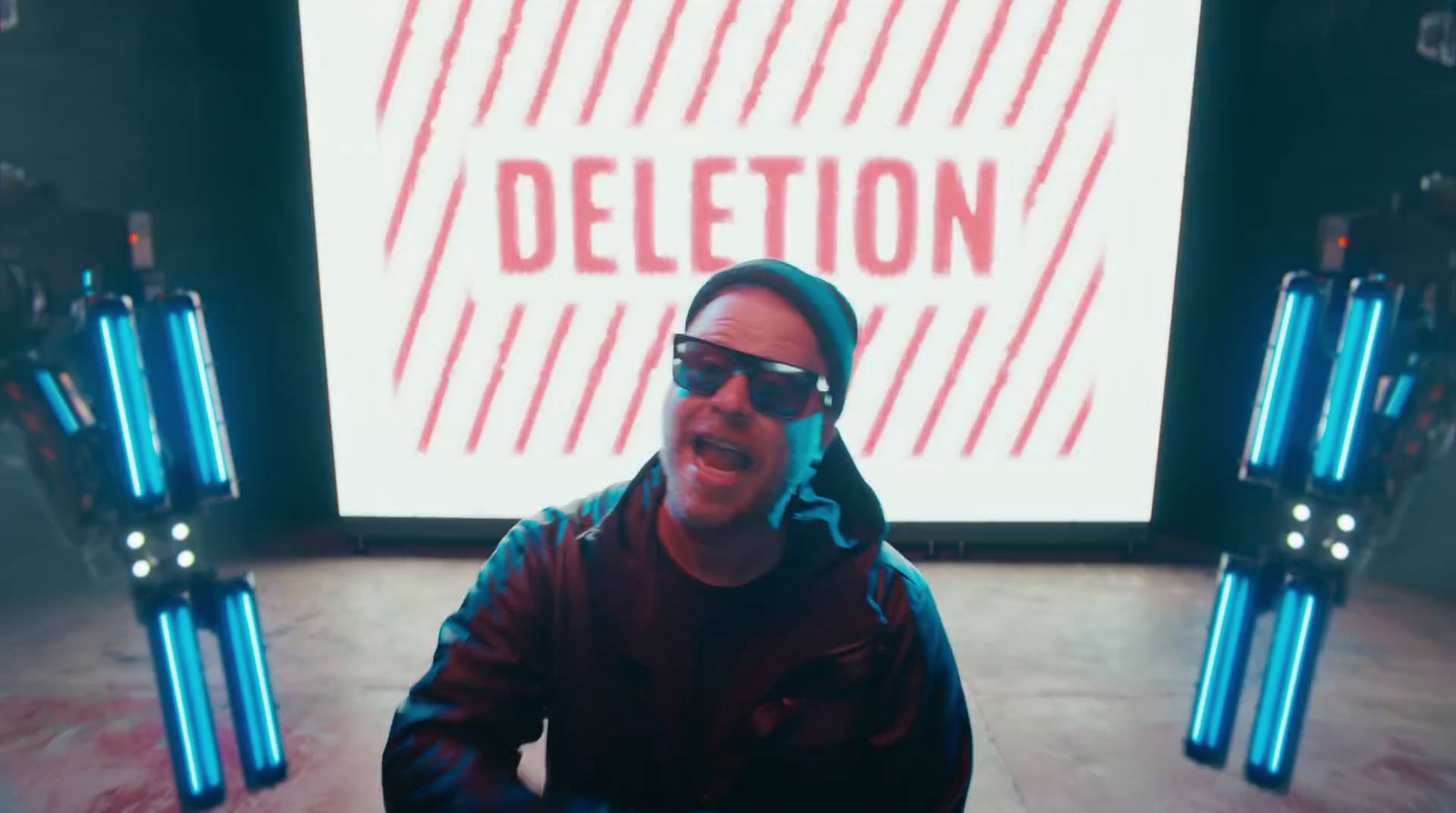 a man wearing sunglasses sitting in front of a projection screen