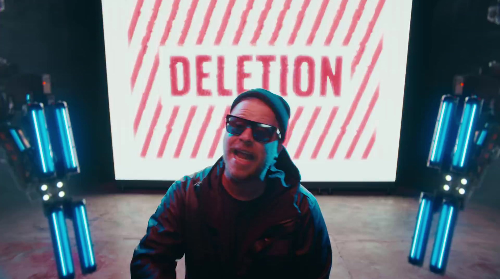 a man wearing sunglasses and a hoodie standing in front of a projection screen