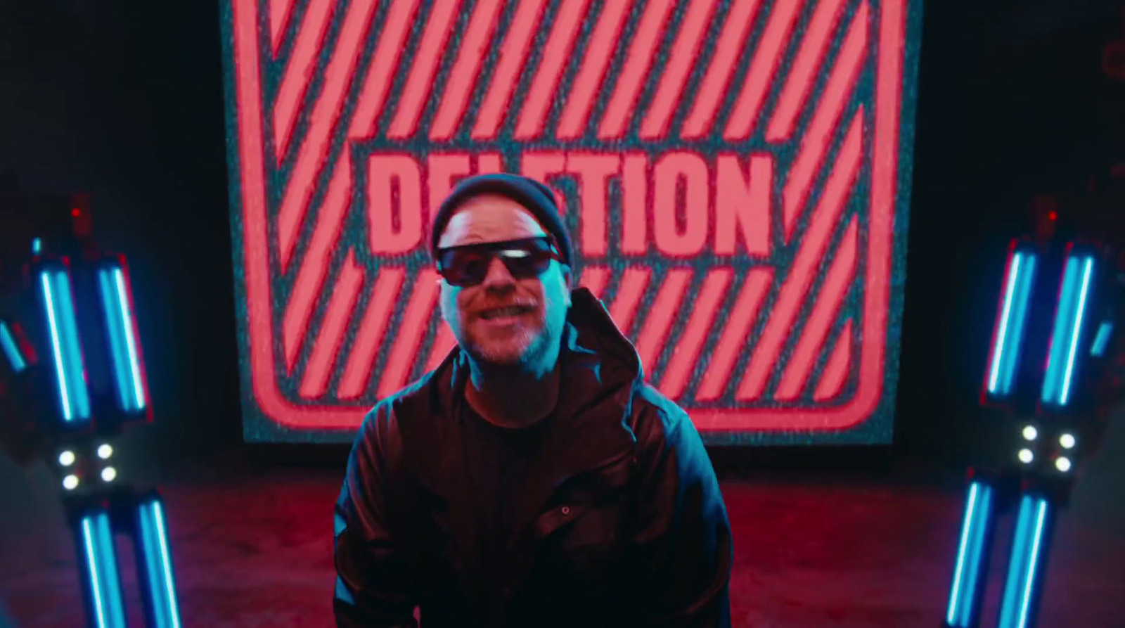 a man wearing a hoodie and sunglasses standing in front of a neon sign