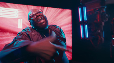 a man in a black jacket and glasses pointing at a television screen