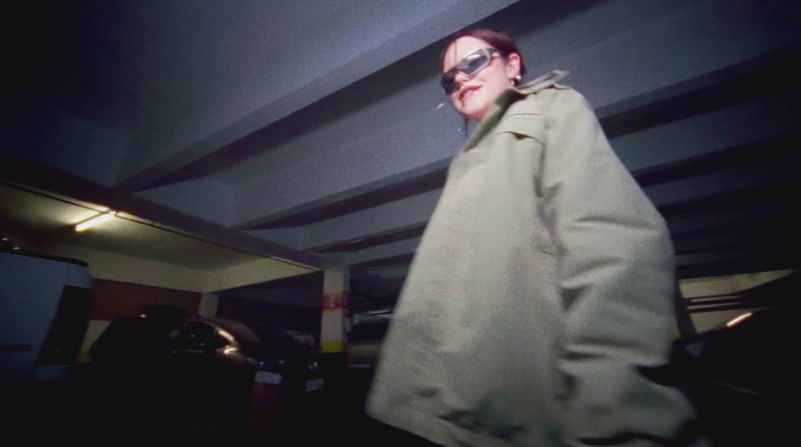 a woman in a trench coat walking through a parking garage