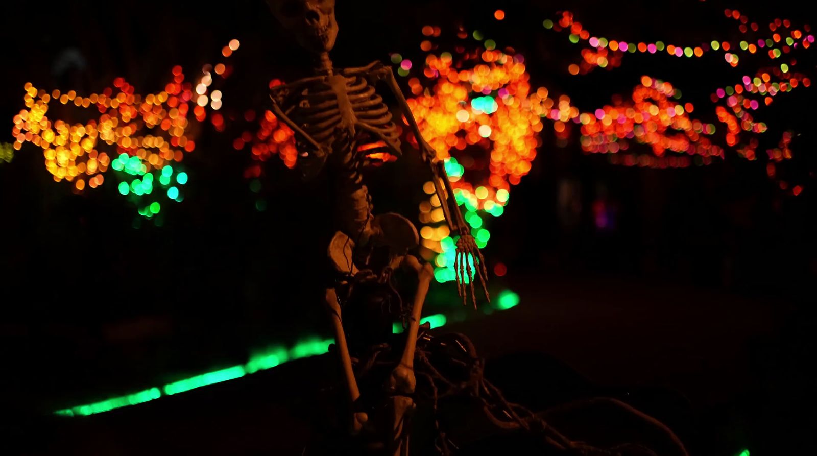 a skeleton sitting on a bike in front of a lot of lights