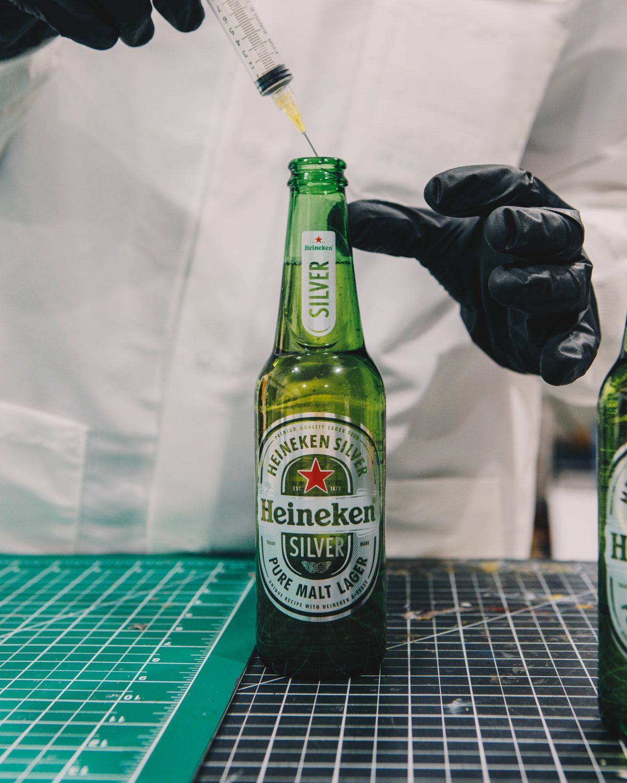 a person in a white coat and black gloves holding a bottle of heineken