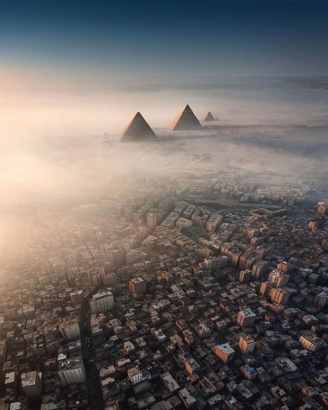 three pyramids rise above a city in the fog