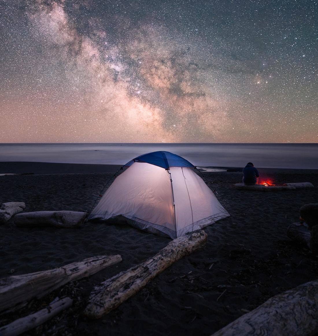 a tent pitched up on a beach under a night sky filled with stars