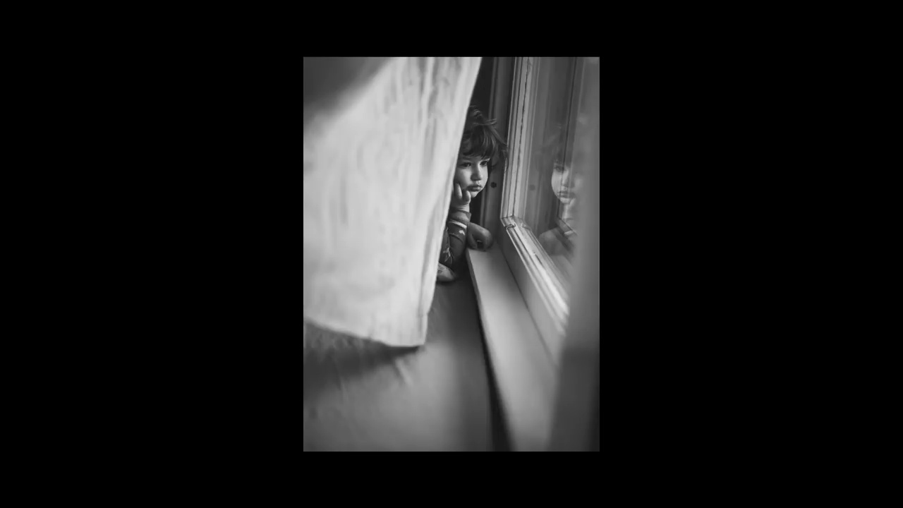 a black and white photo of a child peeking out of a window