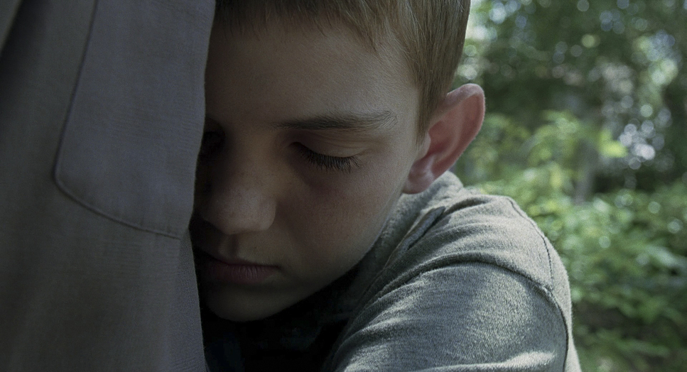 a young boy is holding his head against the back of a jacket