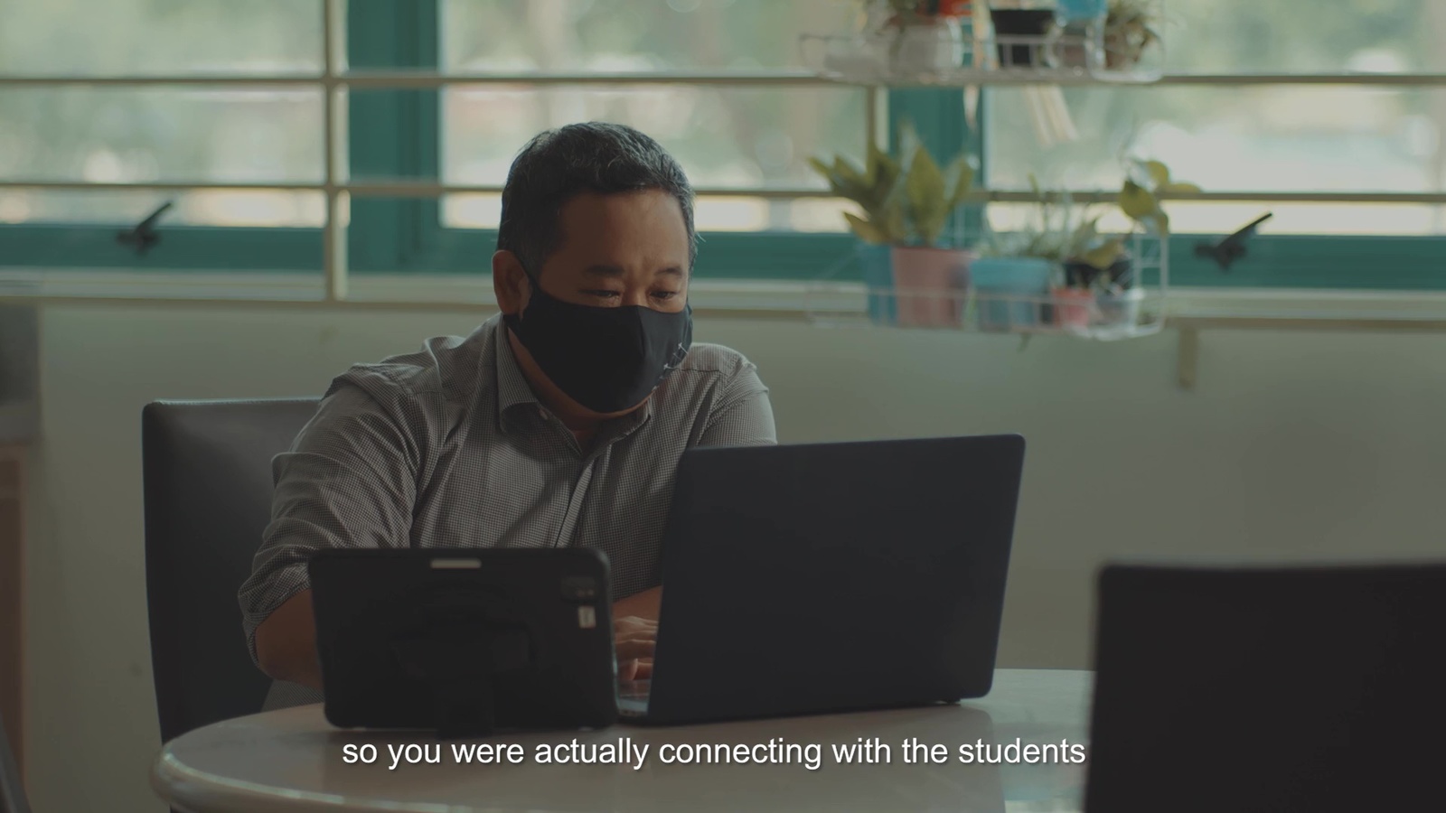 a man sitting at a table with a laptop wearing a face mask