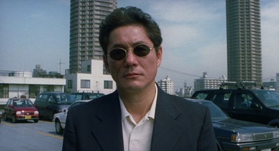 a man in a suit and sunglasses standing in a parking lot