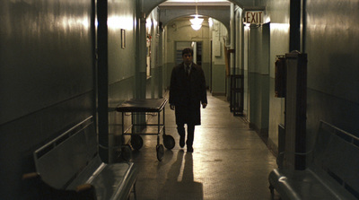 a man walking down a long hallway with a light on