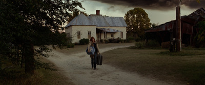 a woman walking down a dirt road towards a house