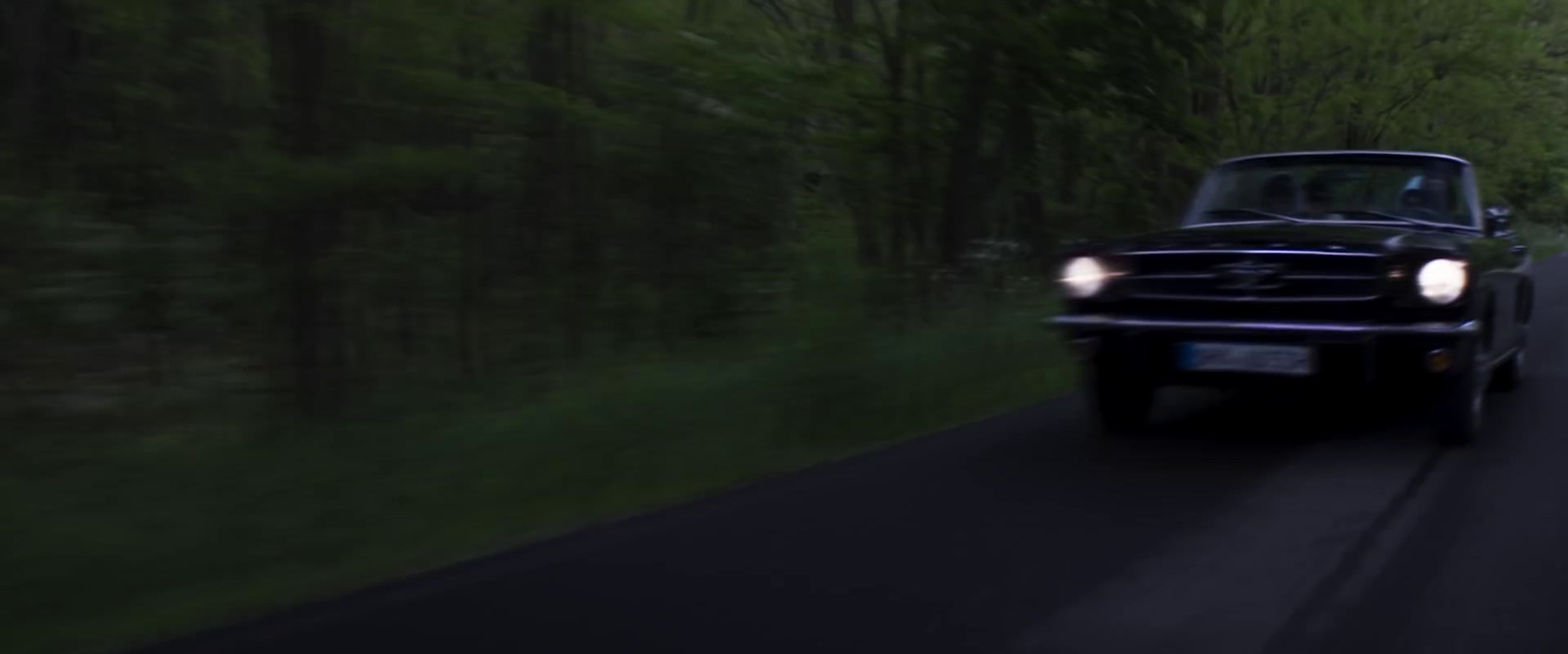 a black car driving down a road next to a forest