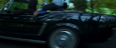 a black car driving down a street next to a forest