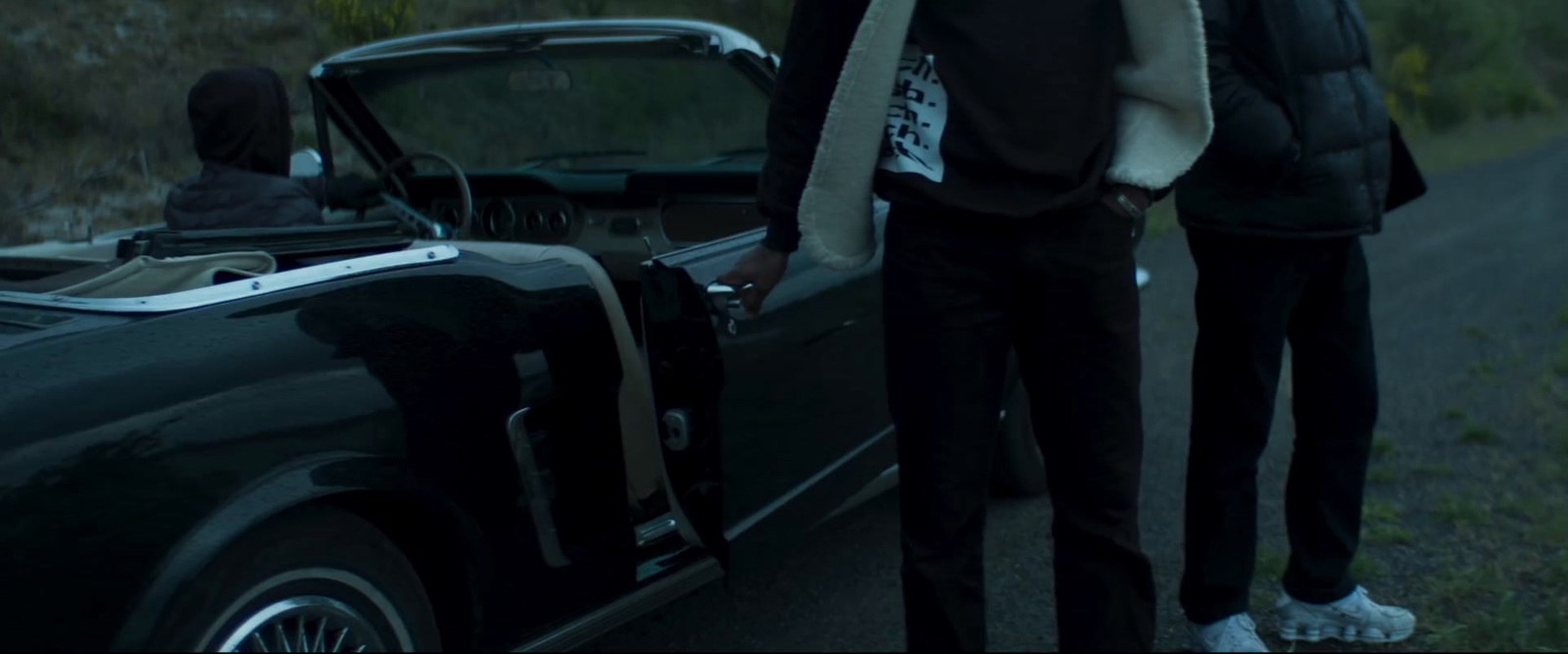 two people standing next to a car on a road