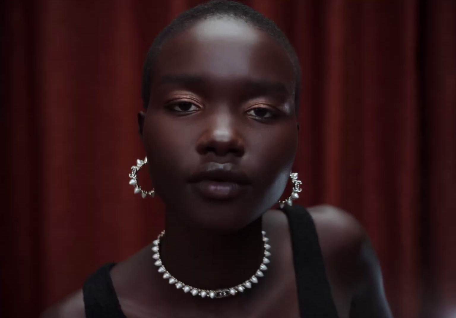 a woman wearing a necklace and earrings in front of a red curtain