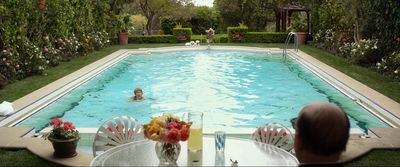 a woman sitting at a table in front of a swimming pool