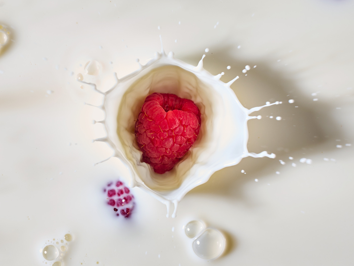 a raspberry in a milk splash on a white surface